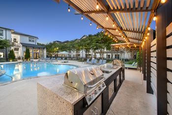 A modern outdoor kitchen with a grill and a pool in the background.